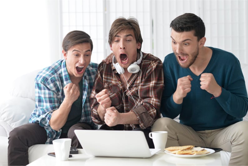 Men excitedly watching a sports event on a laptop