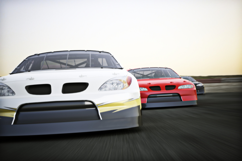 Front view of auto racing race cars racing on a track with motion blur