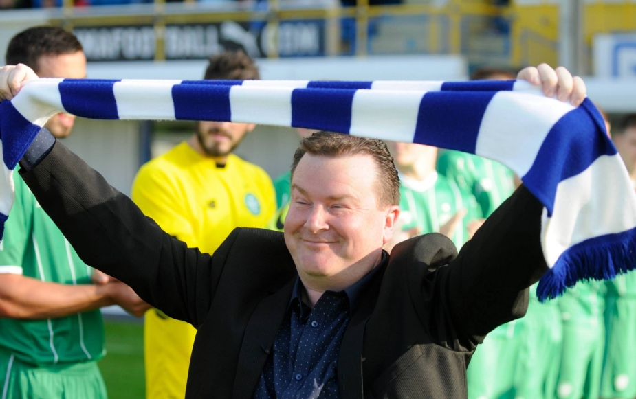 main in suit holding soccer team scarf with arms raised