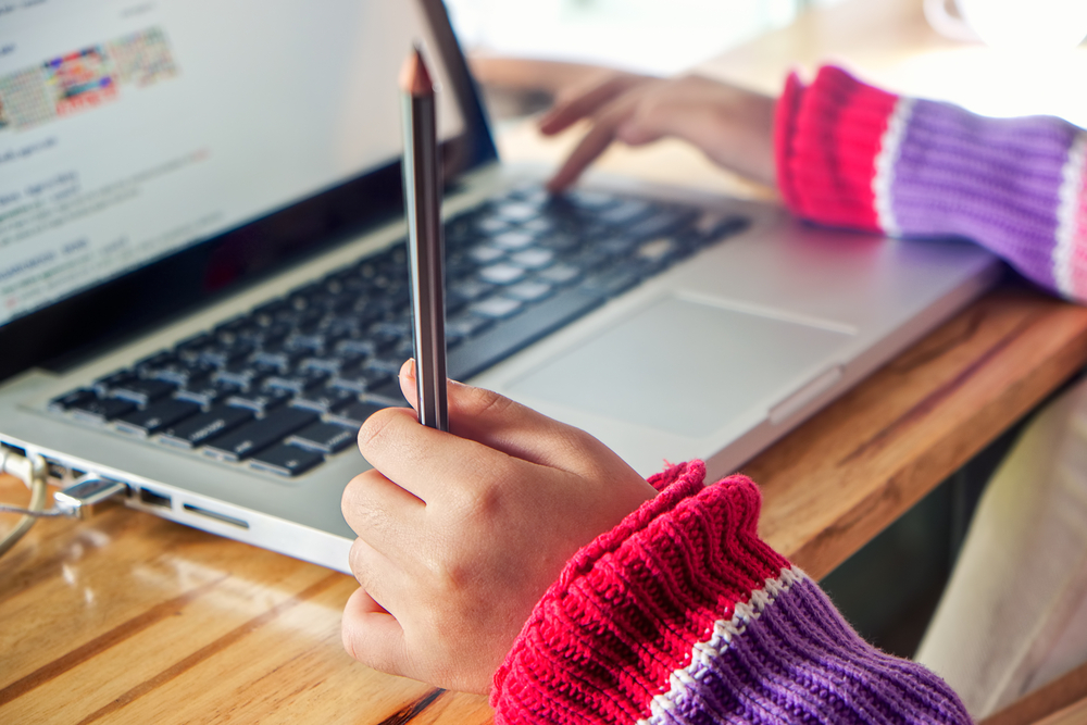 child using a laptop and holding a pencil in one hand