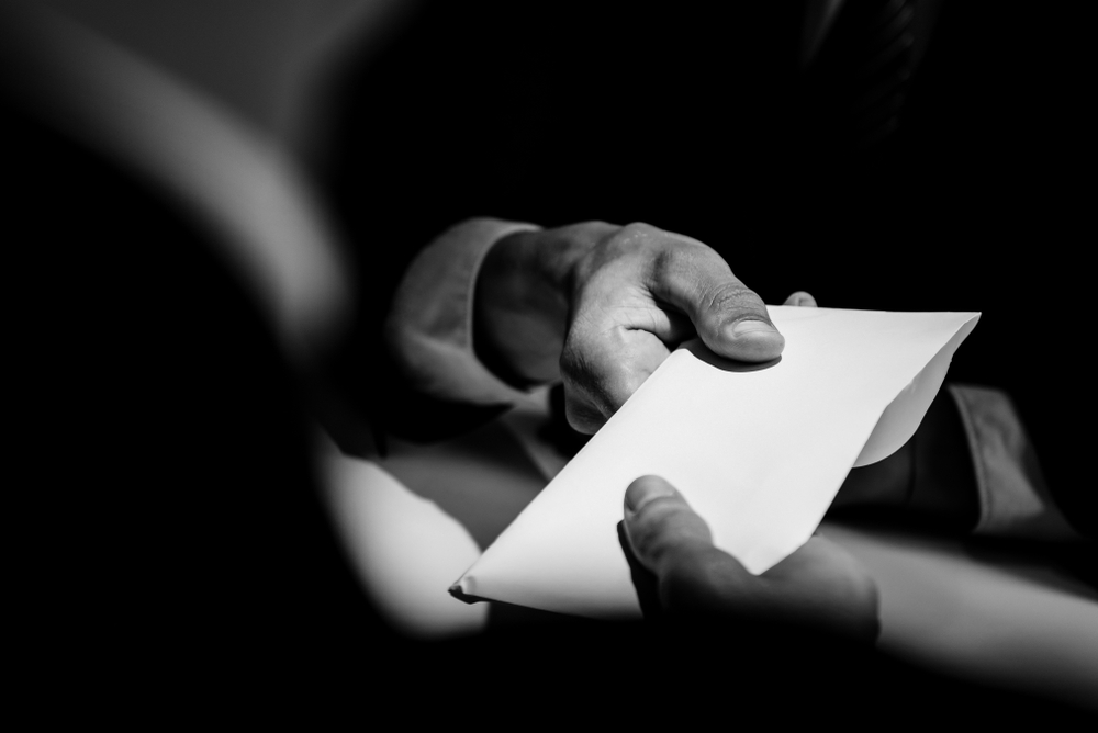 Suited man passing on white envelope to another person