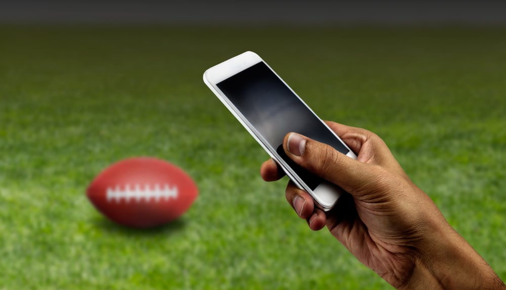 hand holds smartphone with an American football on a field in background