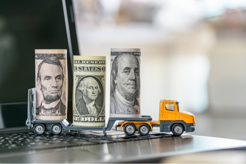 Toy truck on a laptop carrying roles of cash