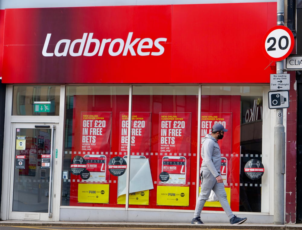 man in a face mask walks past a closed Ladbrokes betting shop in the UK