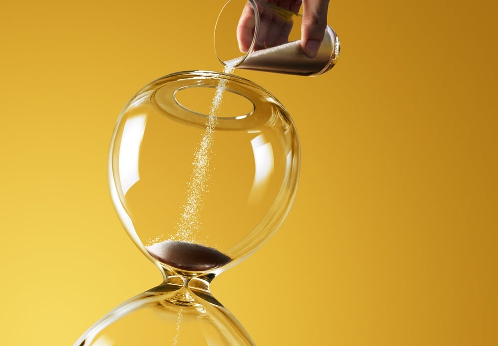 hand pours sand into hourglass