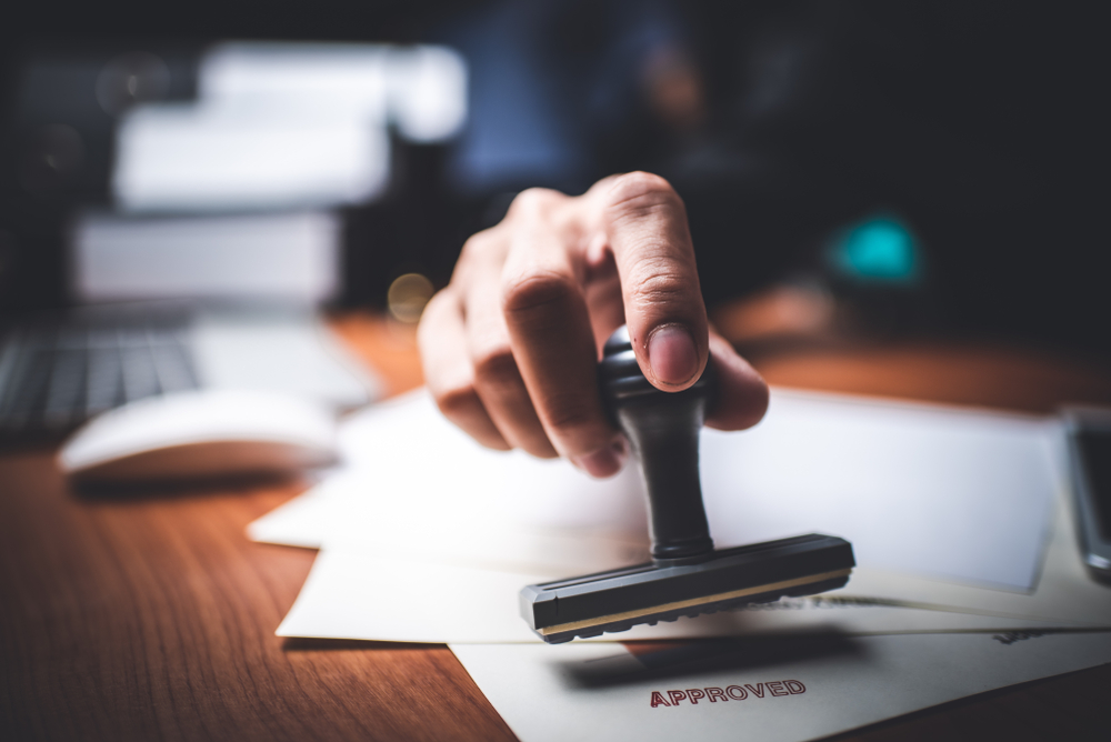 Hand marks document papers with approval stamp on a desk